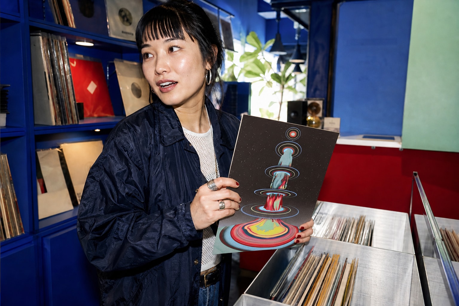 A woman record digger holds Hiver’s Dream Universe sleeve in a colourful record shop